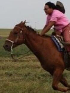 Monica Rattling Hawk riding a horse