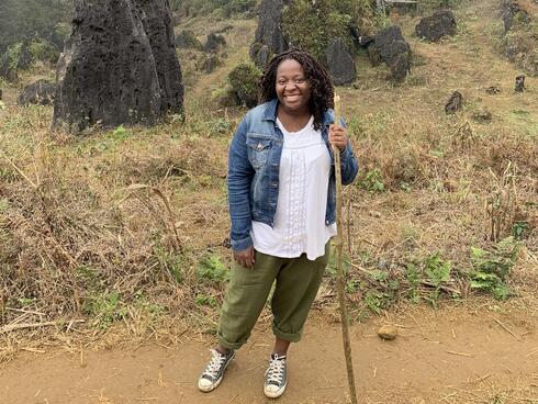 Florence Adewale stands on a trail with a hiking stick in a blue jacket 