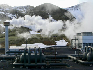 Smoke emits from a pipe at a hydrogen production plant with mountains in the background