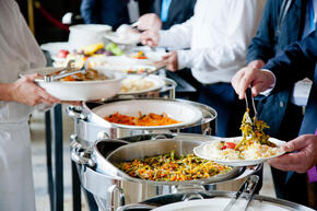 People use tongs to take food from catering trays in a hotel