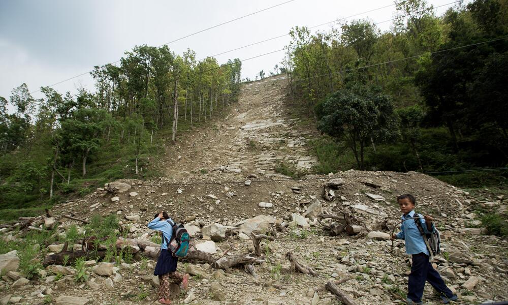 Two children walk in front of a steep dirt slope after a landslide