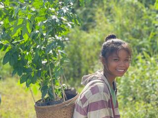 Young girl carrying seedling on her back and smiling in Laos