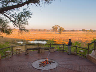 A person stands on a wood deck of Nambwa Lodge, looking out towards the savannah.